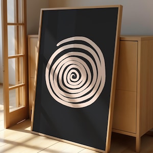Pode incluir: Impressão de arte emoldurada com um design em espiral creme sobre um fundo preto. A obra de arte é exibida em uma moldura de madeira clara, encostada em um armário de madeira. Adiciona um toque moderno a qualquer ambiente.
