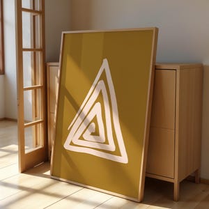 May include: A framed art print with a white abstract triangle design on a mustard yellow background. The artwork is propped against a light wood cabinet and a wooden door frame, creating a minimalist aesthetic.