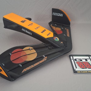 Pode incluir: Modelo preto e laranja de um componente de carro de corrida, com logotipos de patrocinadores como Jack Daniel's e Workday. O design inclui um logotipo Mastercard e o texto "GT 88 3D CARS PRINTED" em um cartão separado.