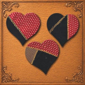 May include: Three heart-shaped fabric ornaments featuring a patchwork design. Each heart combines solid black fabric with red fabric patterned with small white crosses, joined by visible yellow cross-stitch embroidery along the seams.