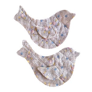 May include: Two bird-shaped fabric decorations. The birds are white with a pattern of small black dots, and floral designs in pink, yellow, and blue. The wings are folded over.