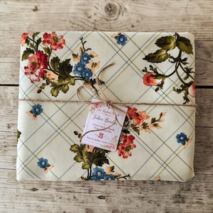 Puede incluir: Un paquete de tela atado con hilo, con una tela color crema con un estampado floral de flores rojas, azules y naranjas. La tela está entrecruzada con un patrón de cuadrícula azul claro. Una etiqueta dice "Fabric Bundles".