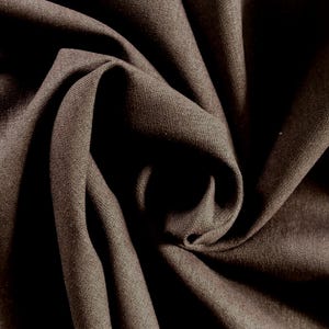 Puede incluir: Primer plano de una muestra de tela marrón con textura y pliegues visibles. La tela es de color liso, con variaciones de luz y sombra que crean profundidad. El material es probablemente adecuado para ropa o decoración del hogar.