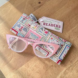 May include: Pink cat-eye reading glasses with a matching patterned case. The case and glasses feature the text "Stitchy Readers" and "To have a friend you must". The case is decorated with colorful postage stamp designs.