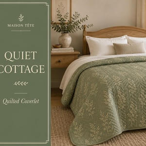 May include: A sage green quilted coverlet featuring a delicate cream-colored botanical pattern of sprigs and leaves. The bedding is draped over a bed with white pillows and a small rectangular beige accent pillow, with text reading MAISON TETE QUIET COTTAGE.