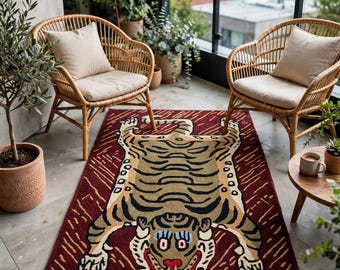 May include: A rectangular area rug featuring a stylized tiger illustration in shades of tan, black, and red against a deep maroon background with gold-colored linear patterns. The rug is positioned between two light brown rattan chairs.