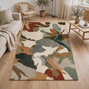 May include: A rectangular area rug featuring an abstract organic pattern with large, flowing shapes in shades of cream, terracotta, sage green, dark forest green, and muted gray. The design consists of layered, curved color blocks.
