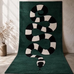 Peut inclure: Un tapis rectangulaire de couleur vert forêt profond présentant un grand motif central représentant un serpent sinueux. Le serpent présente un motif répétitif de larges rayures horizontales noires et blanc cassé sur tout le corps.