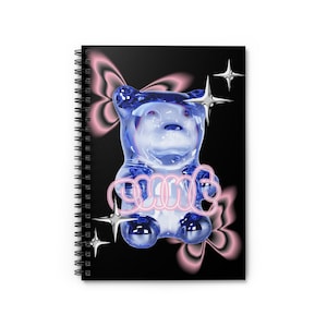 Op de afbeelding: Spiraalgebonden notitieboek met een zwarte kaft met een blauwe gummybeer-illustratie met het woord "PINK" in roze neon. Roze en zilveren steraccenten en een roze vlinderontwerp maken het ontwerp compleet.