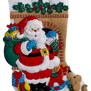 May include: A felt Christmas stocking with the name "Sophia" embroidered in red. The stocking features a Santa Claus design with a sack of toys, a rocking horse, a dog, and a train. The stocking is decorated with holly and berries.