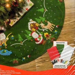 May include: A green felt Christmas tree skirt kit featuring appliqued designs of Santa Claus, a cabin, a deer, pine trees, and fish. The package includes stamped felt, cotton floss, and separated sequins and beads, with a 43 inch diameter indicated.