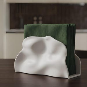 May include: A white napkin holder with an organic, undulating, wave-like shape. The holder is constructed with a smooth, matte finish and contains a stack of folded dark forest green paper napkins that are visible above the top edge.