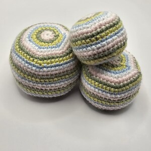 May include: Three handmade crochet balls in pastel colors. The balls are arranged in a small pyramid. The yarn colors include light pink, green, blue, and white. The largest ball has a spiral design on top.