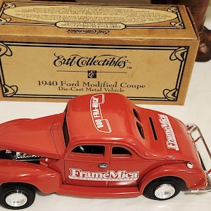 May include: A red die-cast metal 1940 Ford Modified Coupe model car with the text "FrameMica" and "800 FRA-MICA". The model car is in front of a cardboard box with the text "Ertl Collectibles" and "1940 Ford Modified Coupe".