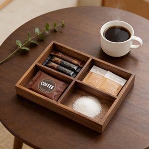 May include: A wooden serving tray with six compartments, holding coffee packets, sugar, and coffee stirrers. A white mug filled with black coffee sits nearby. The tray is on a dark brown wooden table.