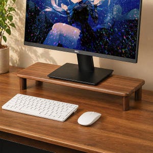 May include: A wooden monitor stand with a dark brown finish. A white keyboard and mouse sit on the desk in front of the stand. The stand is supporting a black monitor with the brand name "HKC" visible.