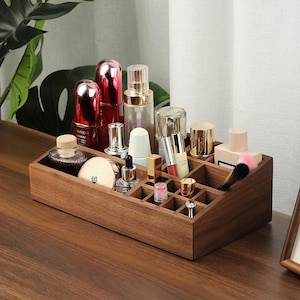 May include: A wooden makeup organizer with multiple compartments, filled with various cosmetic products. The organizer is made of dark brown wood and sits on a wooden surface. The cosmetics include bottles, lipsticks, and brushes.