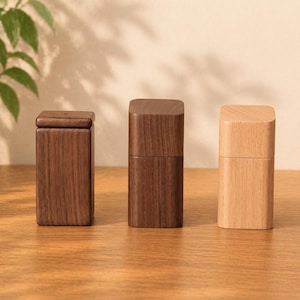 May include: Three wooden boxes in varying shades of brown and tan. The boxes are rectangular with rounded corners and a lid or top. The wood grain is visible, and the boxes are arranged on a light brown surface.