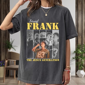 Puede incluir: Camiseta gris oscuro con el nombre "Forrest Frank" en letras amarillas. Debajo, un collage de imágenes y el texto "THE JESUS GENERATION". La imagen central muestra a una persona con un micrófono, con el número 83 en la camiseta.