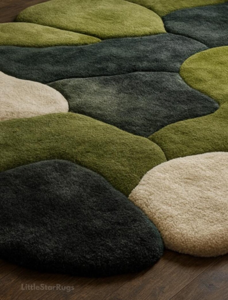 K&ouml;nnte beinhalten: Nahaufnahme eines Teppichs mit Kieselstein-Design. Der Teppich weist verschiedene Gr&uuml;n-, Beige- und Schwarzt&ouml;ne auf und erzeugt einen nat&uuml;rlichen, organischen Look. Der Teppich besteht aus einem weichen, strukturierten Material.