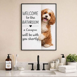 Peut inclure: Un panneau de salle de bain encadré avec le texte "WELCOME to the BATHROOM" et "a Cavapoo will be with you shortly." Un chien Cavapoo apparaît derrière le panneau. Le panneau est au-dessus d'un lavabo de salle de bain avec des articles de toilette.