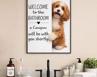 May include: A framed bathroom sign with the text "WELCOME to the BATHROOM" and "a Cavapoo will be with you shortly." A Cavapoo dog peeks out from behind the sign. The sign is above a bathroom sink with toiletries.