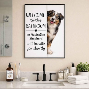 May include: Framed bathroom wall art with the text "WELCOME to the BATHROOM" and "an Australian Shepherd will be with you shortly." The art features a smiling Australian Shepherd dog. The art is framed in a black frame.