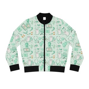 Peut inclure: Veste de bombardier vert clair avec col, poignets et ourlet noirs. La veste présente un motif répété de fournitures médicales, notamment des stéthoscopes, des seringues et des gants. Veste de style décontracté et léger.