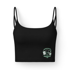 Könnte beinhalten: Schwarzes Crop-Top mit dünnen Trägern. Das Oberteil hat eine hellgrüne Grafik mit medizinischen Symbolen und den Worten "asistencia médica". Das Design umfasst ein Stethoskop, einen Klemmbrett und andere medizinische Symbole.