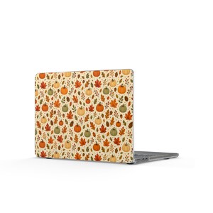 Può includere: Un computer portatile dotato di una pellicola protettiva con un motivo ripetuto di zucche arancioni, verdi e color crema, foglie autunnali e piccole ghiande su uno sfondo color crema chiaro, che copre l'intero coperchio esterno.
