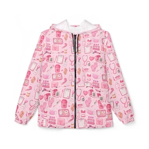 Peut inclure: Veste à capuche rose avec un motif répété d'articles médicaux, tels que des stéthoscopes, des seringues et des masques. La veste a une fermeture éclair noire et une doublure blanche dans la capuche.
