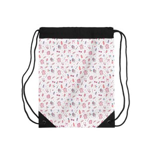 Könnte beinhalten: Ein weißer Kordelzugbeutel mit schwarzem Oberteil und schwarzen Kordeln. Der Beutel ist mit einem sich wiederholenden Muster aus rosa OP-Kleidung, Stethoskopen, Sonnenbrillen, Schleifen und anderen medizinischen Illustrationen bedeckt.