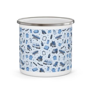 May include: White enamel mug with a silver rim, featuring a repeating pattern of medical equipment and supplies in shades of blue. The design includes ambulances, wheelchairs, and medical charts, creating a healthcare theme.