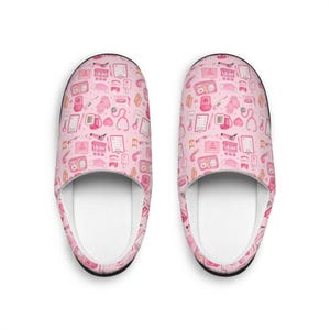 May include: A pair of pink slippers with a repeating pattern of medical-themed illustrations. The pattern includes stethoscopes, thermometers, and medical charts. The slippers have a white interior and a black trim.