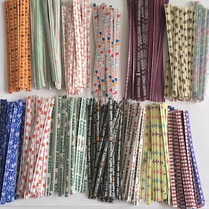 May include: A collection of colorful paper twist ties in various patterns. Designs include snowflakes, hearts, and holiday greetings. Some ties have text that reads "BAKERY FRESH" and "HAPPY HOLIDAYS".
