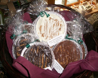 Può includere: Un cesto di vimini pieno di diverse torte confezionate. Le torte sono in vaschette di alluminio e coperte da cellophane trasparente, legate con un nastro verde. Le torte hanno un tema burro di arachidi e cioccolato, con glassa bianca.