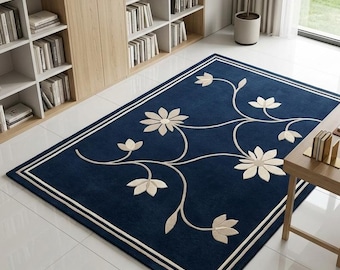 Könnte beinhalten: Ein rechteckiger Teppich mit tiefblauem Hintergrund, einem cremefarbenen Blumenrankenmuster und einer doppelten Umrandung. Der Teppich liegt auf einem weißen Fliesenboden in einem Raum mit einem Holzregal und einem Schreibtisch aus Holz.