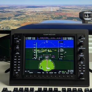 May include: A black flight deck display showing flight data, including altitude, heading, and navigation information. The screen displays a green circular gauge and other flight details. The text "FLIGHT DECK DIY" is visible. A keyboard is in the foreground, with a landscape visible in the background.