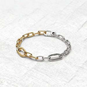 May include: A two-tone chain bracelet. One half is gold-coloured, and the other is silver-coloured. The bracelet features a clasp closure and a series of oval and rectangular links. The bracelet is displayed on a white surface.