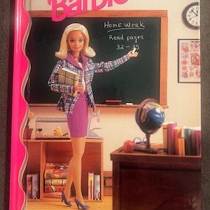 Peut inclure: Couverture de livre Barbie intitulée "The Class Act". La couverture présente une poupée Barbie habillée en enseignante, devant un tableau noir avec des instructions de devoirs. L'arrière-plan comprend un globe, des livres et une horloge.