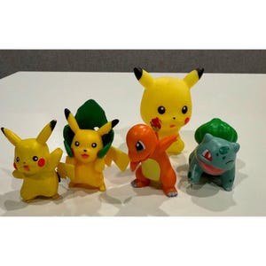 May include: A collection of six colorful Pokémon figurines. The figures include Pikachu, Charmander, and Bulbasaur, in various poses. The figurines are made of plastic and are brightly colored.