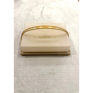 May include: A rectangular, off-white plastic food storage container with a matching base and a removable, arched yellow handle. The handle features a series of circular cutouts along its length, and the container has a smooth, opaque finish.