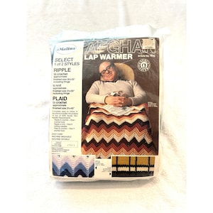 May include: A Malina brand craft kit for an Afghan lap warmer in a plastic package. The packaging features a person with glasses sitting in a chair with a chevron-patterned blanket, with text detailing ripple and plaid style options.