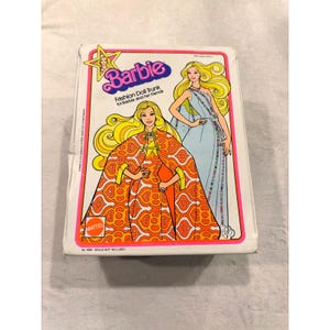 Puede incluir: Un baúl de muñeca Barbie Fashion vintage con ilustraciones de Barbie con trajes de moda. El baúl presenta el logotipo de Barbie y el texto "Fashion Doll Trunk for Barbie and her friends". La combinación de colores incluye rosa, naranja y azul.