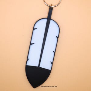 May include: A 3D-printed feather keychain with a white and black design. The keychain has a silver ring and a black strap. The text "3D Feathers Feather Keychain" is at the top. The Sugar Shack HQ is printed at the bottom.