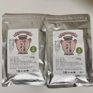 May include: Two identical silver metallic pouches of Hojicha powder, each containing 100g. The white labels feature a pink illustration of a tea jar, Japanese text, and the words Hojicha Powder, Type A, and Marukyu Koyamaen Co., Ltd.