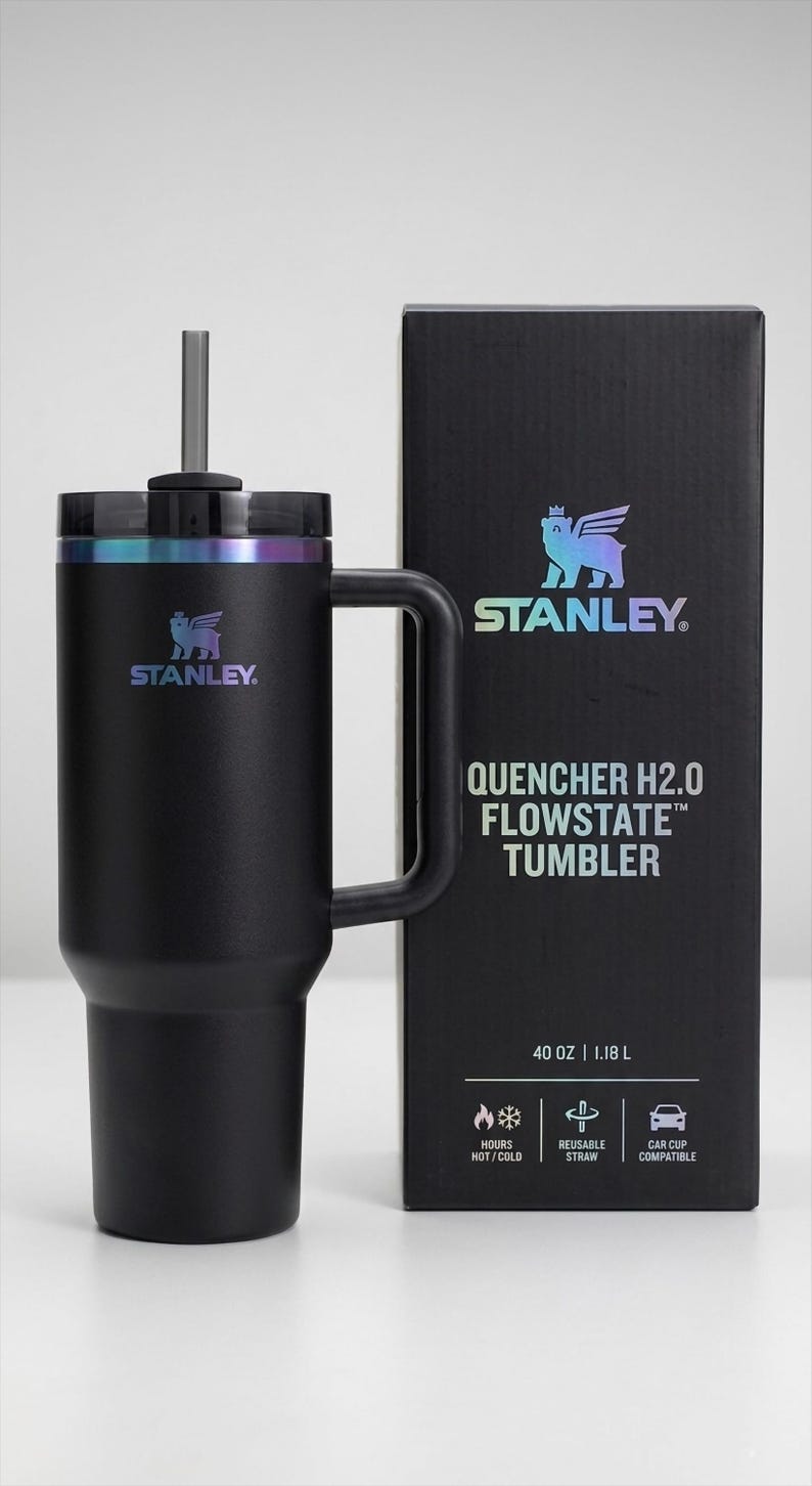 Puede incluir: Vaso Stanley Quencher H2.0 Flowstate negro con asa y pajita reutilizable. El vaso tiene una capacidad de 1,18 L y es compatible con portavasos de coche. El logotipo de Stanley es visible.