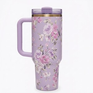May include: A lavender insulated tumbler with a handle and a floral design featuring pink and purple roses and other flowers. The tumbler has a matching lavender handle and lid, and a gold band near the top.