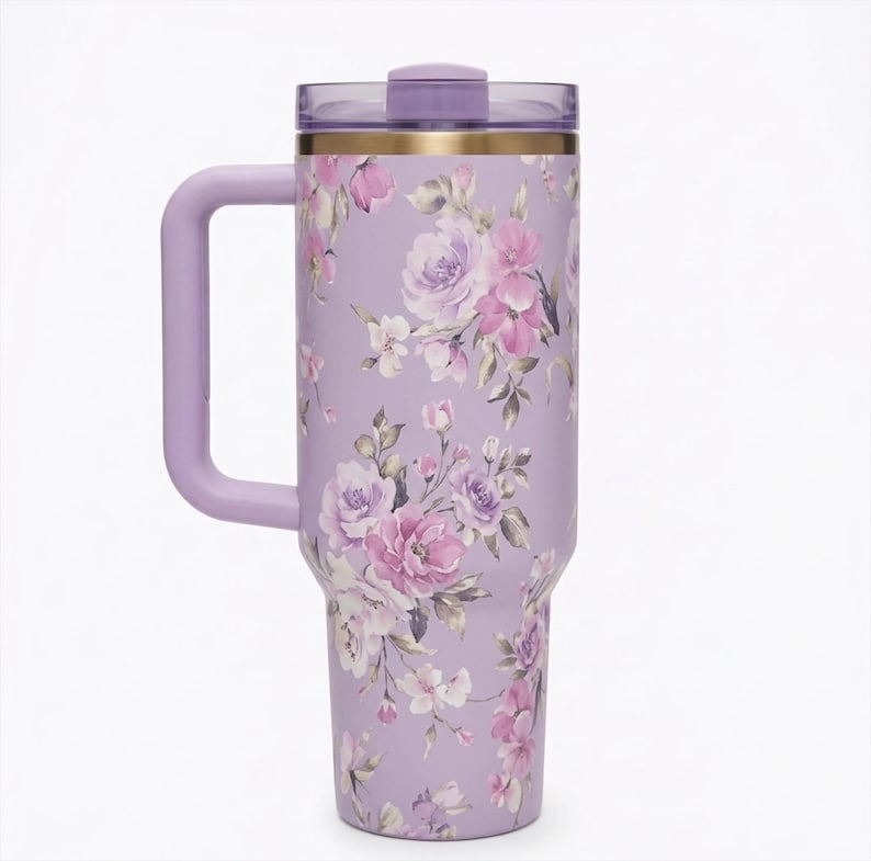 May include: A lavender insulated tumbler with a handle and a floral design featuring pink and purple roses and other flowers. The tumbler has a matching lavender handle and lid, and a gold band near the top.