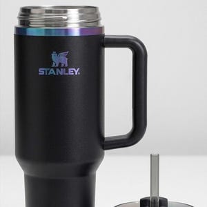 Puede incluir: Vaso t&eacute;rmico negro con asa y tapa. El vaso tiene un borde de acero inoxidable con un acabado iridiscente arco&iacute;ris. El logotipo de Stanley est&aacute; impreso en la parte delantera. La tapa y la pajita est&aacute;n separadas.